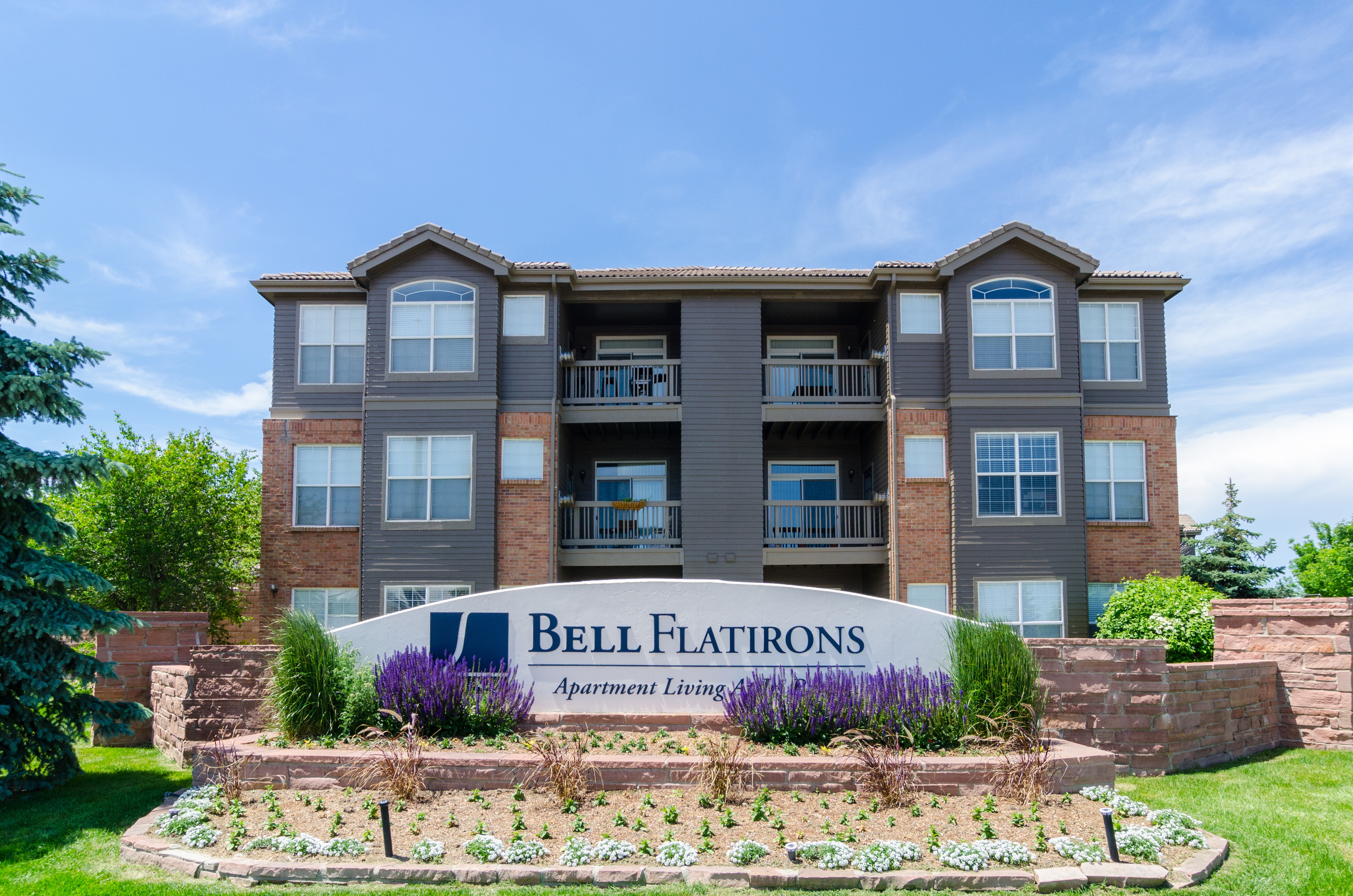 A sign that says Bell Flatirons with a building behind it.